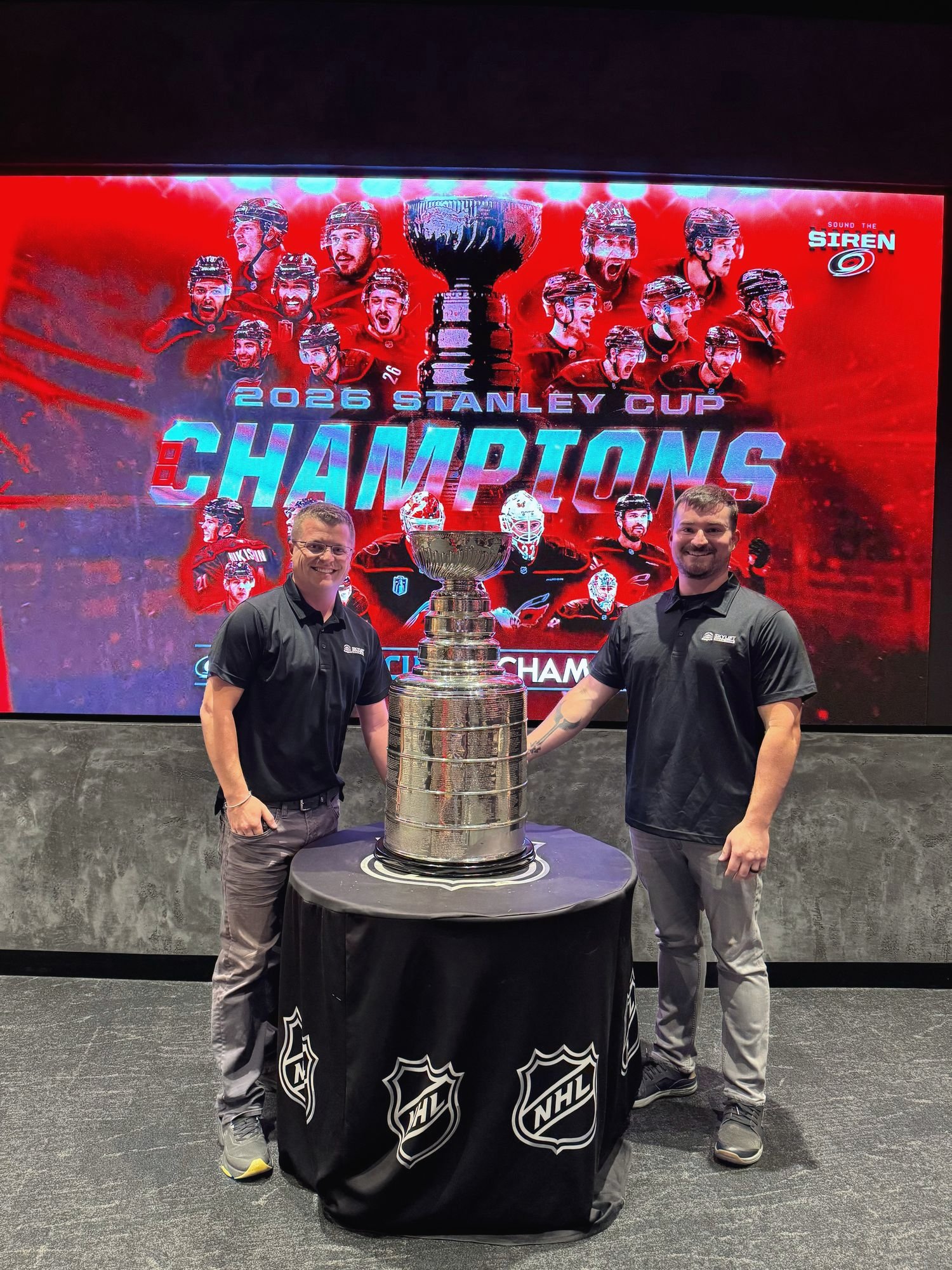 Alex and one other person beside the Stanley Cup in front of a Carolina Hurricanes champions screen